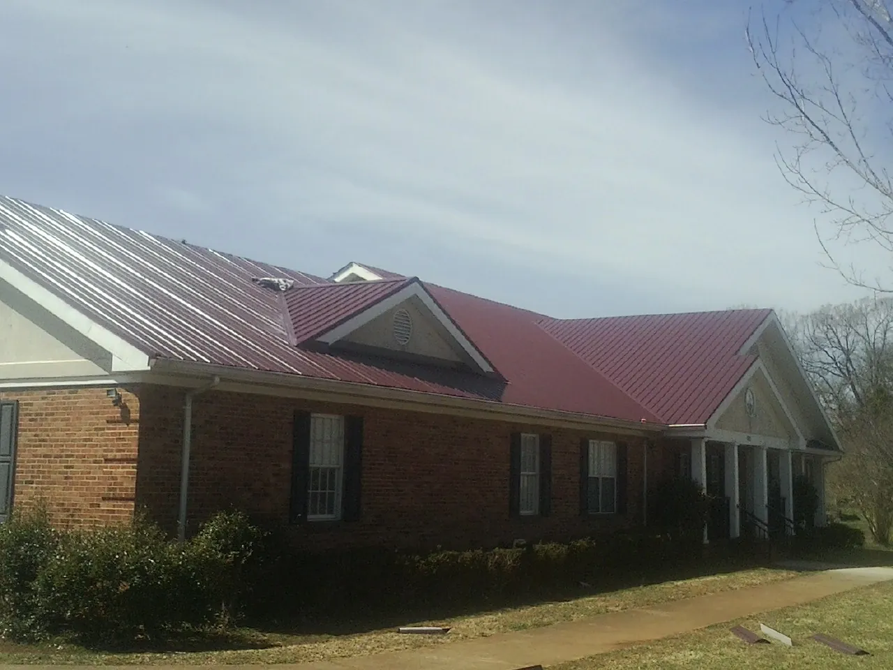 Red metal roof with gabled entries on a long brick building, from a Hail Damage Roof Repair job in Quilcene