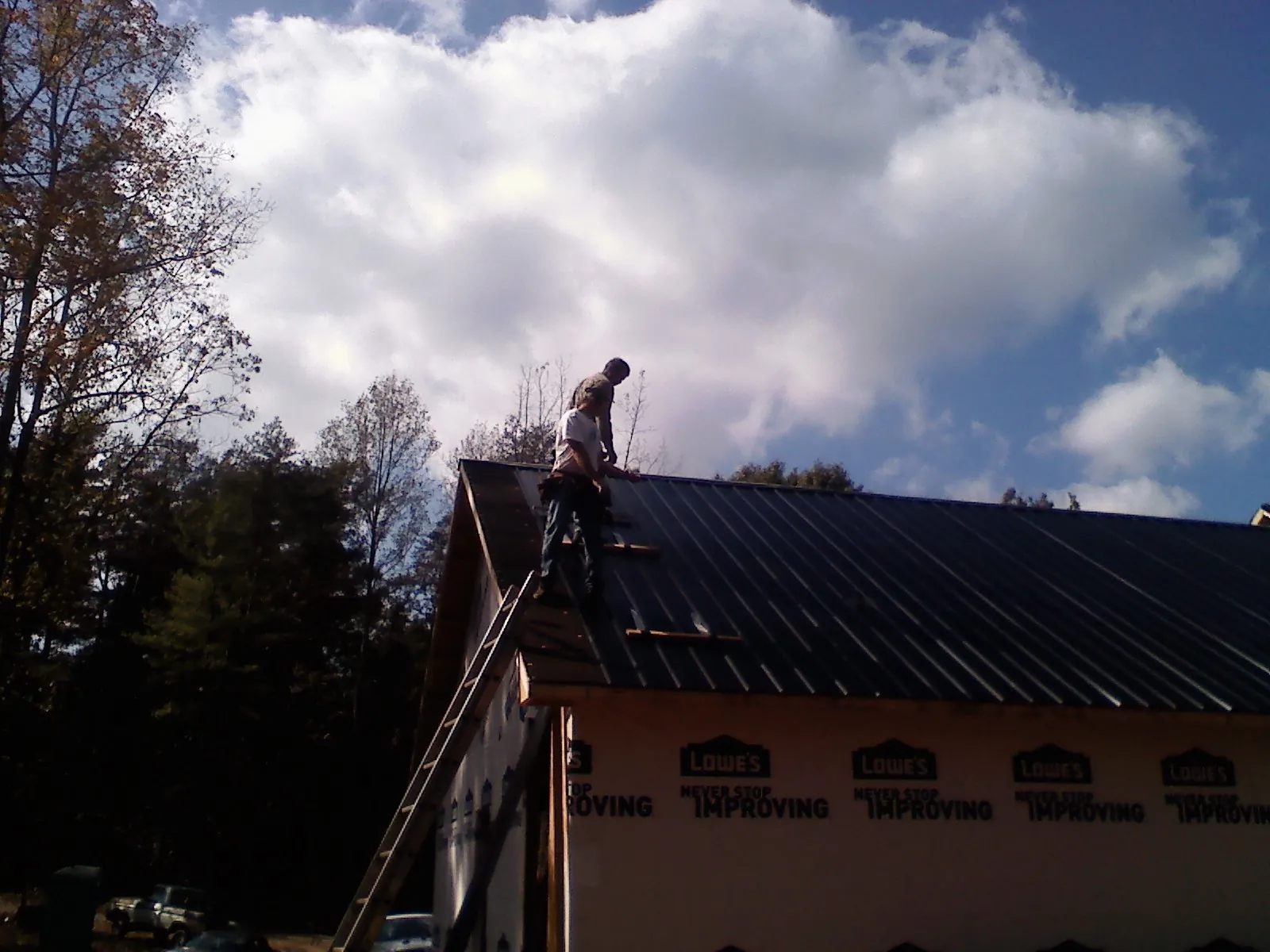 Roofer fastening dark metal panels high against a cloudy sky, from a Roof Inspection job in Quilcene