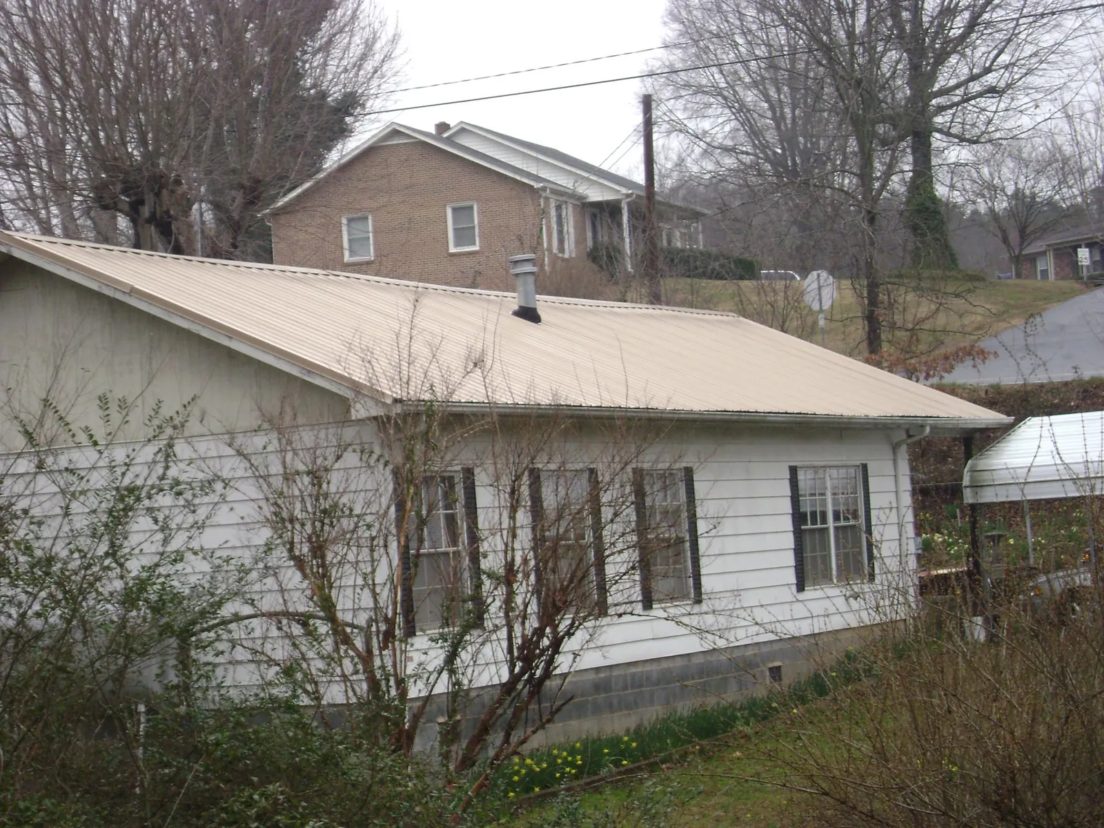 Tan metal roof on a white sided house set into a hillside — Commercial Roofing by Roofing Brothers in Quilcene